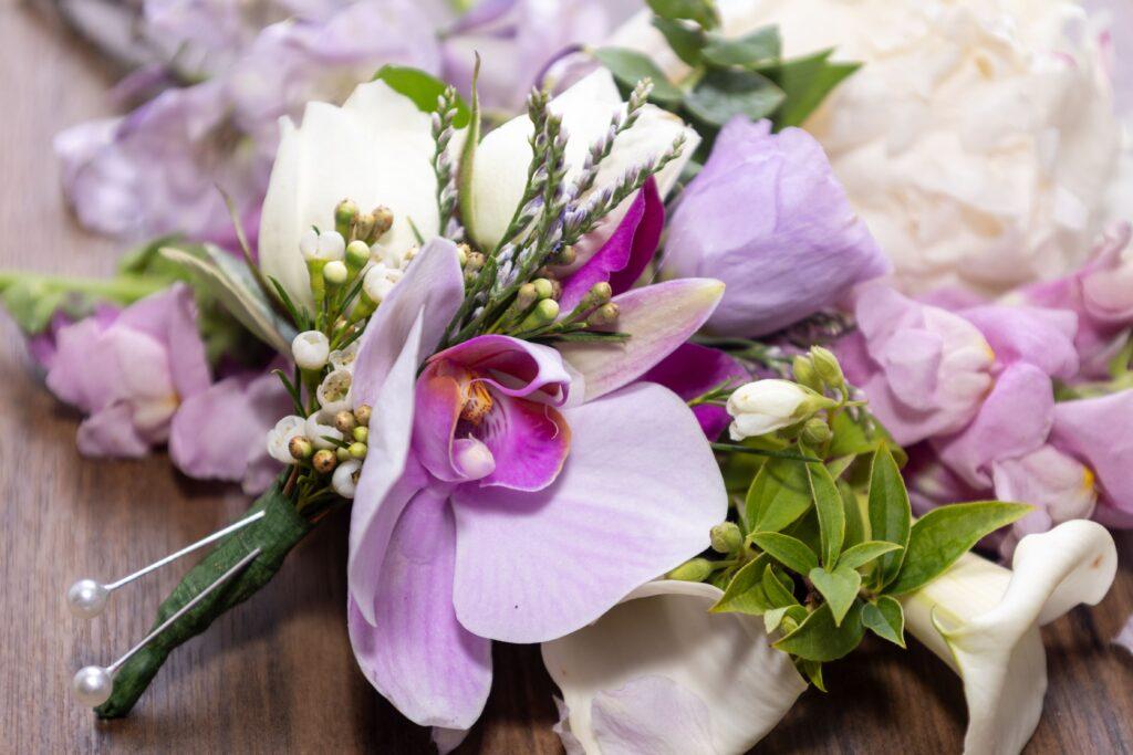 Wedding boutonniere featuring a lavender orchid, white rosebuds, small berries, and fresh greenery.
