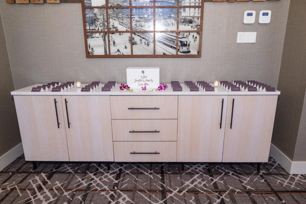 Purple wedding place cards arranged beside Catrenia and John’s white card box and purple orchid accents.